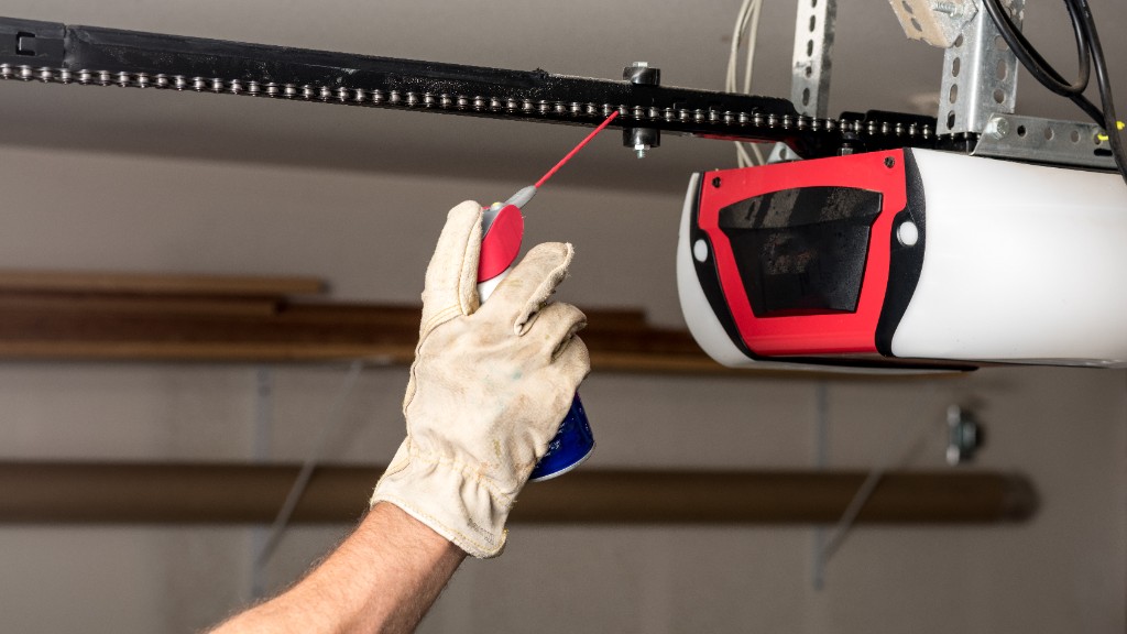 Mano con guante blanco lubricando con aceite rojo la cadena de un motor de puerta de garaje automática blanca y roja