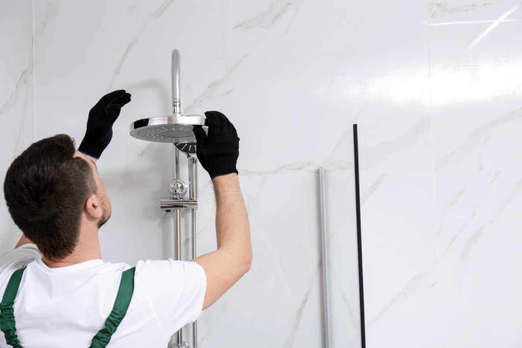 Trabajador con guantes negros instalando cabezal de ducha cromado en pared de marmol blanco veteado en baño moderno